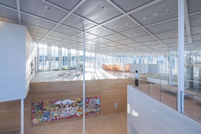 Interior gallery space with white structural grid ceiling and timber-clad walls in bright daylight