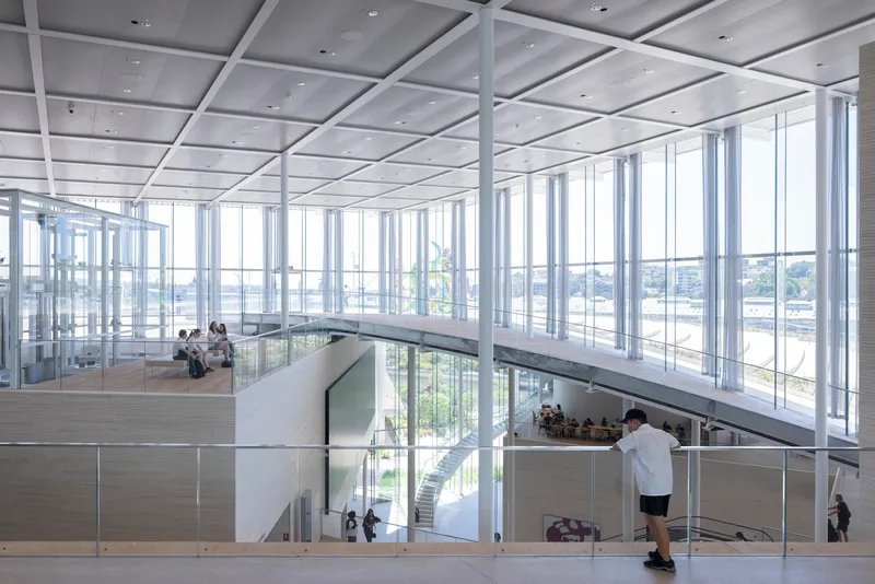 Upper level gallery with floor-to-ceiling glazing overlooking tiered spaces and visitors below