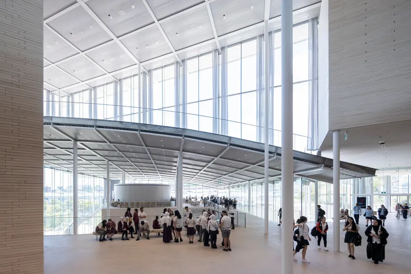 Double-height entrance hall with coffered ceiling, steel mezzanine and floor-to-ceiling glazing with visitors gathering below