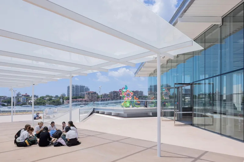 Exterior rooftop terrace with white slatted canopy and glass facade overlooking the waterfront on a partly cloudy day