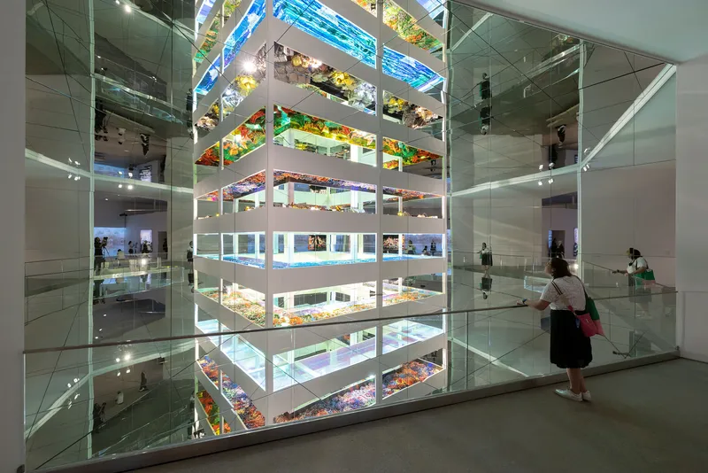 Stacked glass display cases filled with colorful objects viewed by a visitor in the gallery space