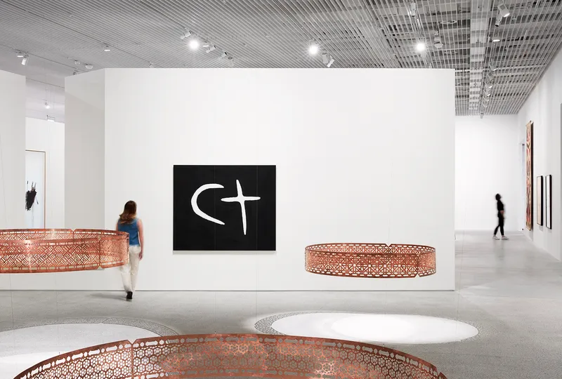 Gallery space with exposed metal ceiling grid, white walls, sculptural installations and two visitors moving through
