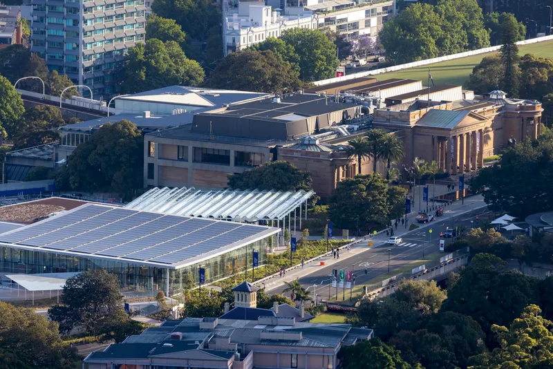 Aerial view showing the angular metal roof volumes nestled among trees and adjacent to a columned classical building