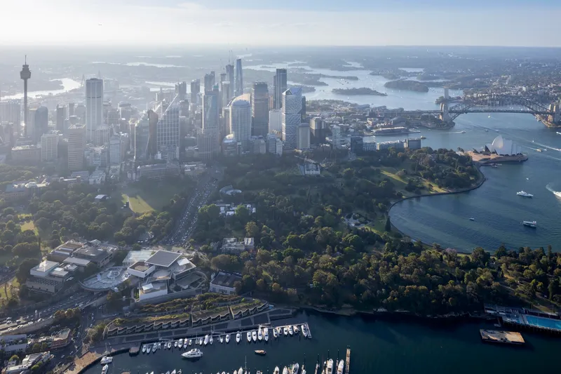 Aerial view of a harbor peninsula with parklands adjacent to a downtown skyline across the water