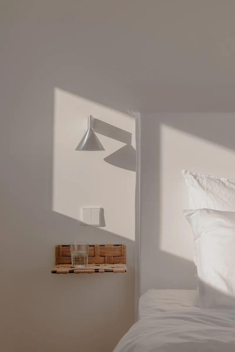 Bedroom alcove with wall-mounted sconce casting geometric shadow across white walls at midday