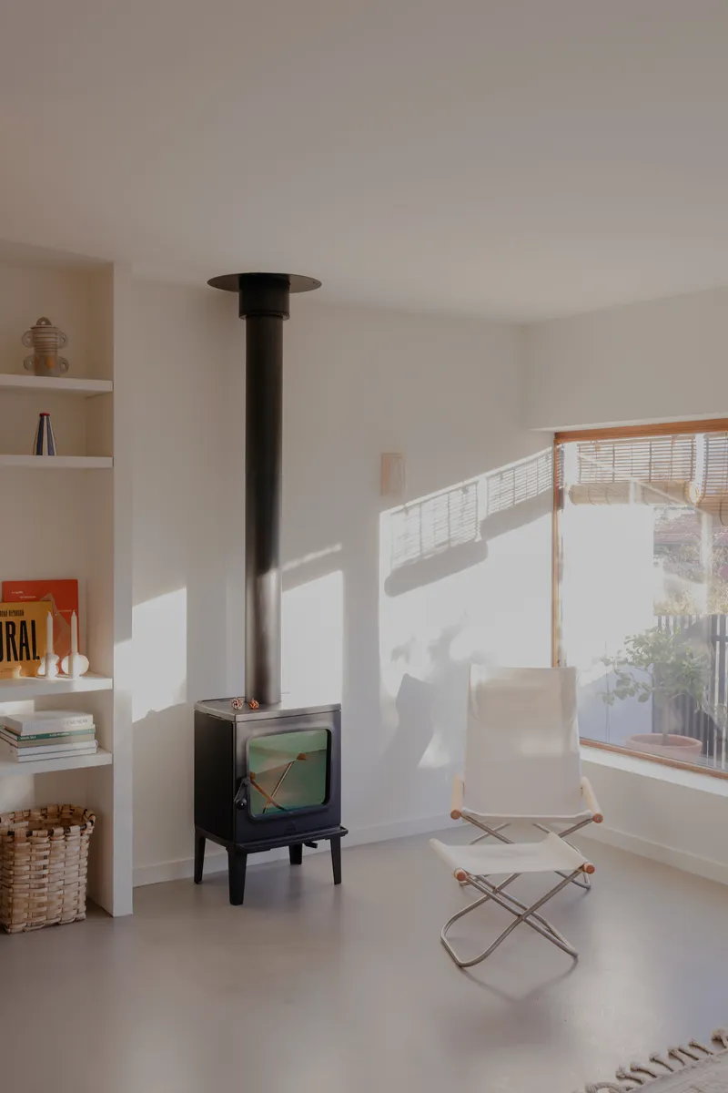 Black freestanding wood stove beside canvas lounge chair with afternoon sun casting window shadows on white walls