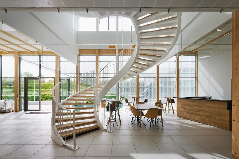 Double-height lobby with a helical staircase in white steel and timber treads under skylights