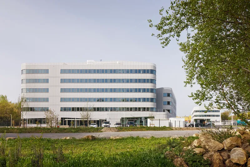 Horizontal striped facade of six-story office building viewed across wild grasses and boulders