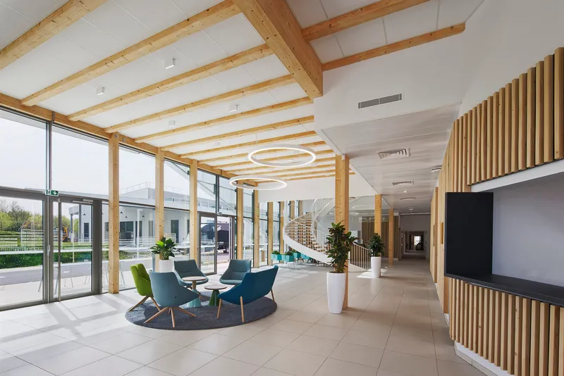 Lobby with exposed timber beams and vertical wood slat screens beside a seated cluster