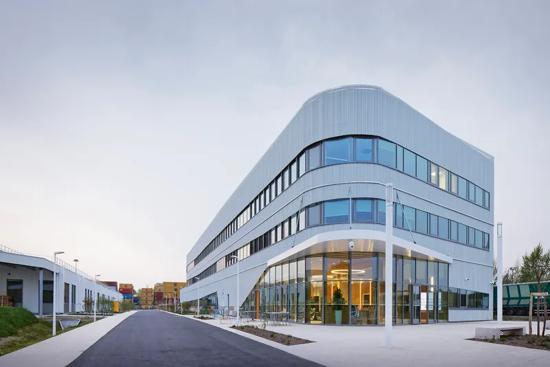 Curved corner entry facade with floor-to-ceiling glass and ribbed metal cladding at dusk