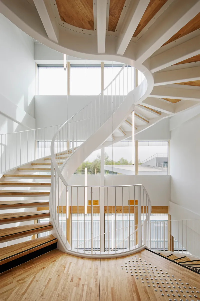 Spiral staircase with white metal railings and timber treads rising through a multi-story atrium