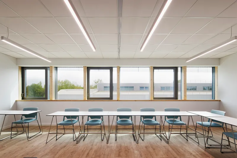 Conference room with a long white table, grey chairs and rhythmic timber-framed windows overlooking spring trees