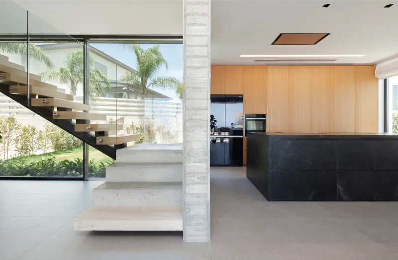 Open kitchen with black marble island adjacent to floating concrete stair and glass balustrade