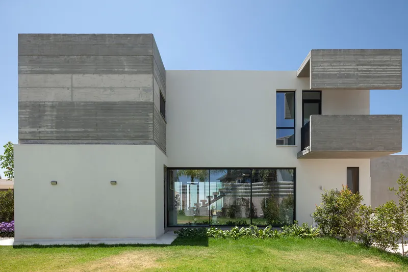 Garden facade showing interlocking white stucco and board-formed concrete volumes under blue sky