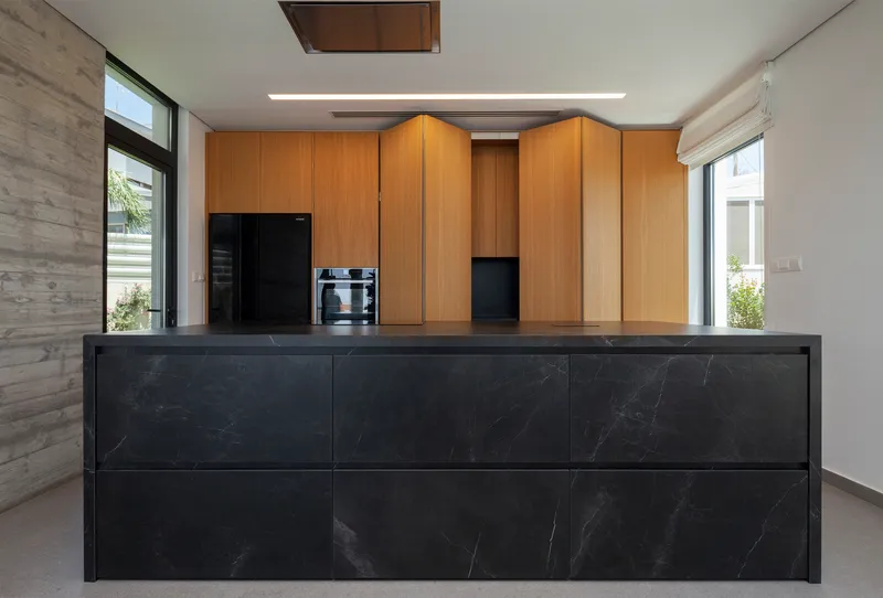 Kitchen island clad in dark marble with wood cabinetry beyond and flanking windows