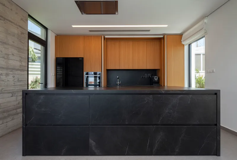 Open wood cabinetry revealing dark backsplash and sink with marble-clad island in foreground