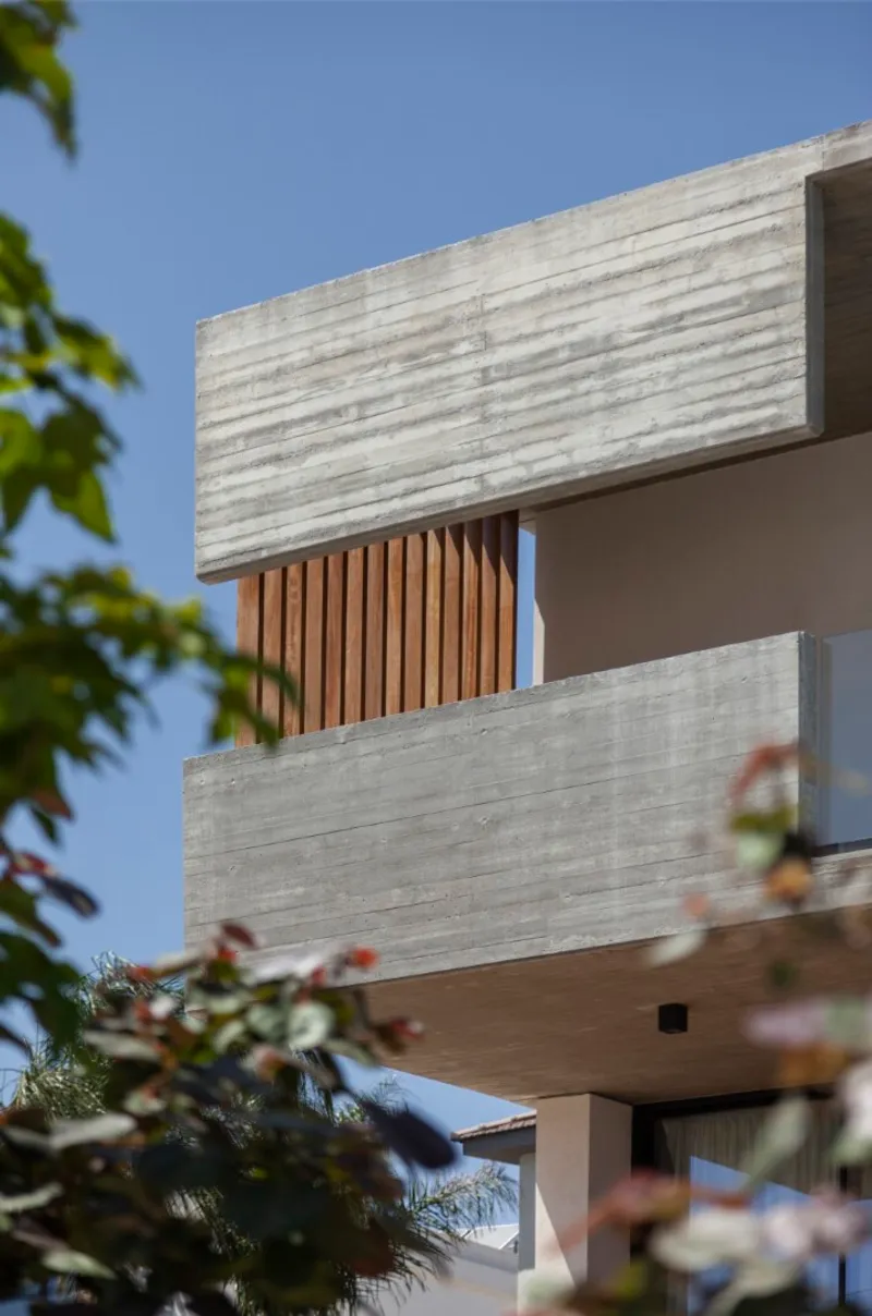 Stacked concrete volumes with vertical timber screening seen through foliage against a clear blue sky