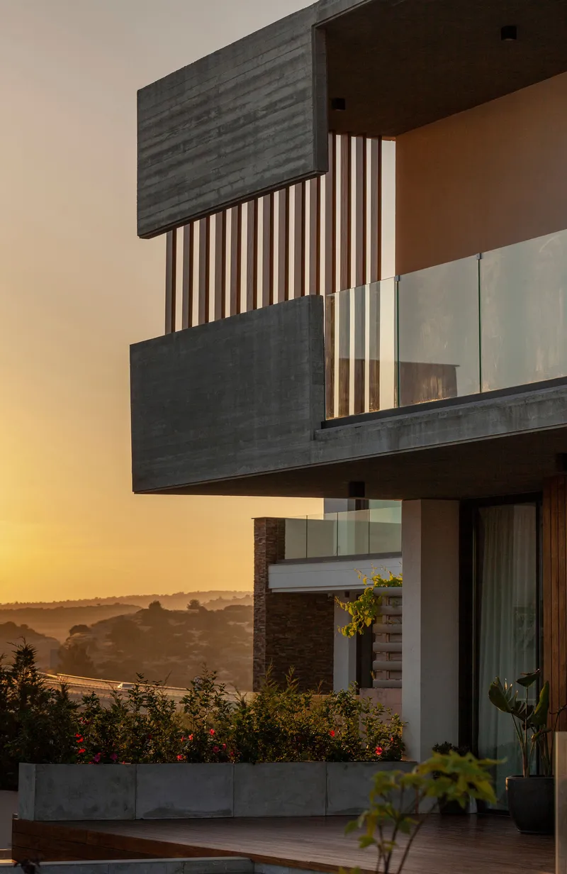 Cantilevered concrete balconies with timber screens at sunset overlooking planted terraces and distant hills