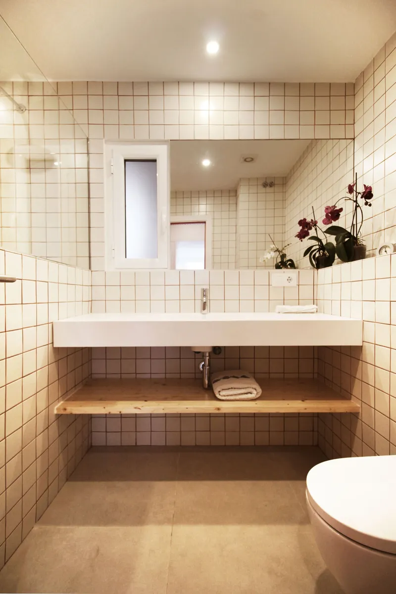 Bathroom with cream square tile walls, wall-hung sink, timber shelf below and recessed mirror cabinet