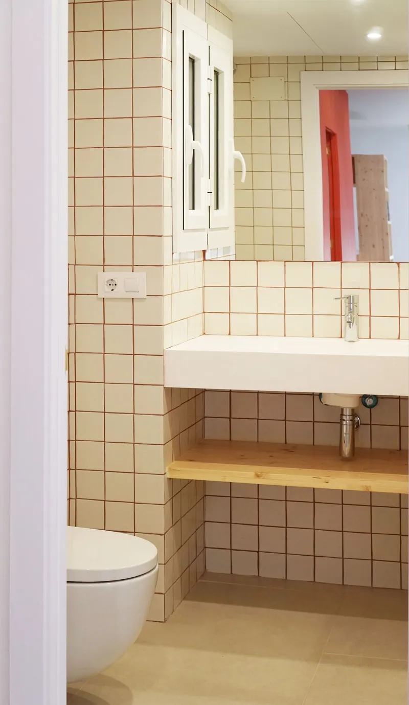 Bathroom corner showing cream tiled walls, white sink with timber shelf and reflection in medicine cabinet mirror