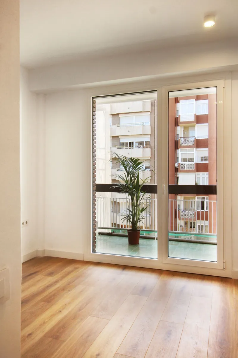 White interior room with timber flooring and glazed door opening to balcony with potted plant
