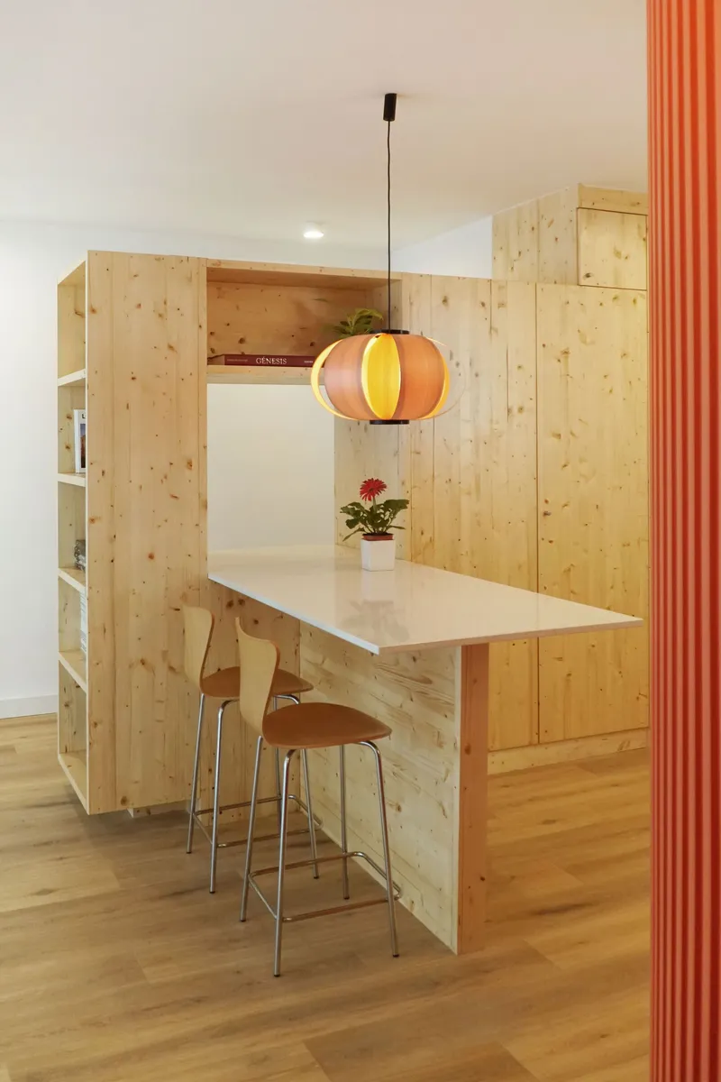 Kitchenette with timber cabinetry, white counter, bar stools and pendant lamp beside red corrugated panel