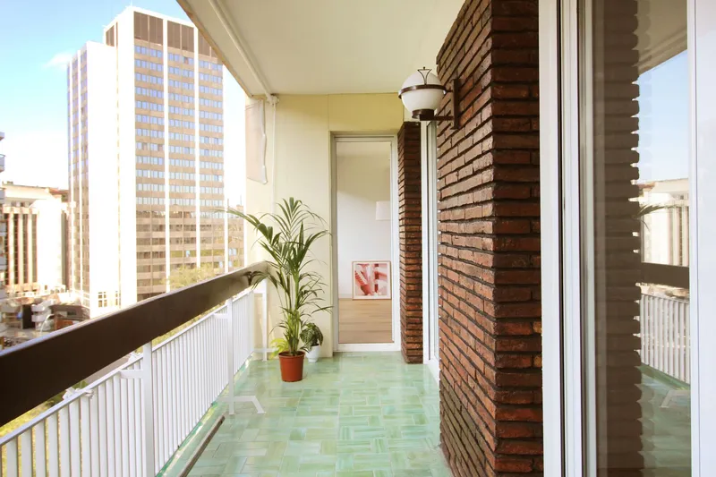 Covered balcony with green mosaic tile floor and brick screen wall beside tall residential towers