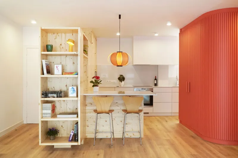 Open-plan kitchen with pine shelving unit and fluted orange cabinet wall in recessed lighting