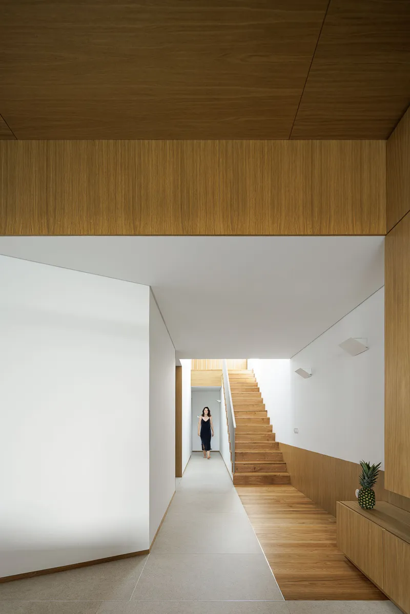 View along white corridor toward timber staircase with figure standing at entry threshold