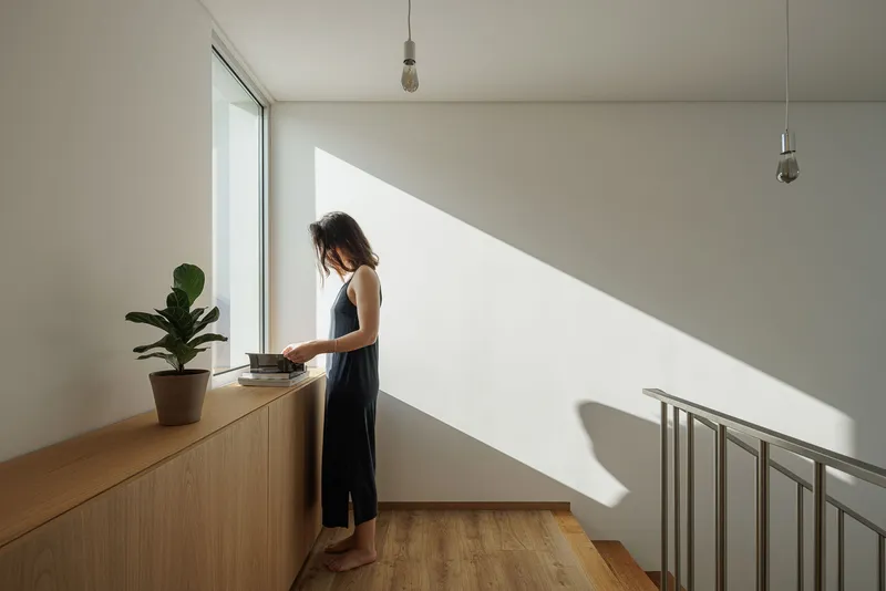 Upper landing with low timber counter beside window casting sharp diagonal sunlight across white wall