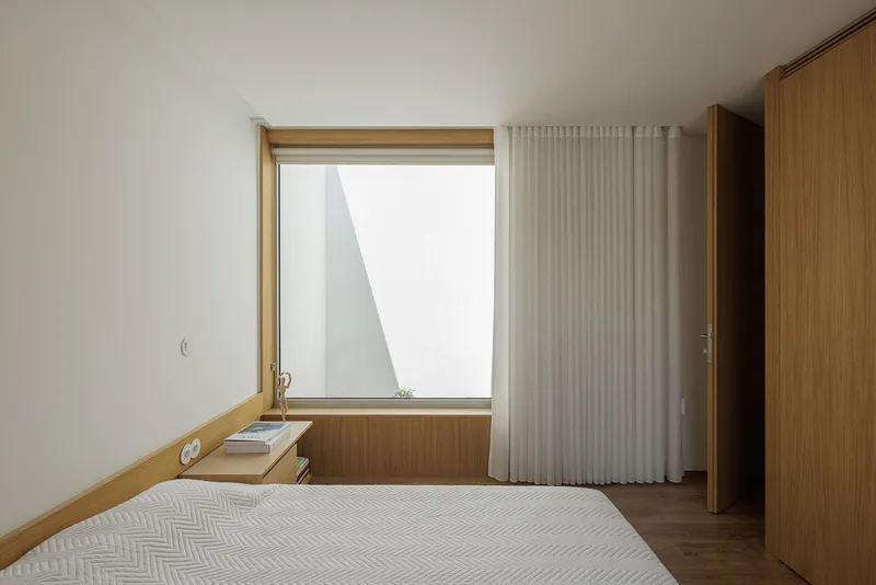 Bedroom with timber-framed window and white curtain partially drawn beneath sloped ceiling