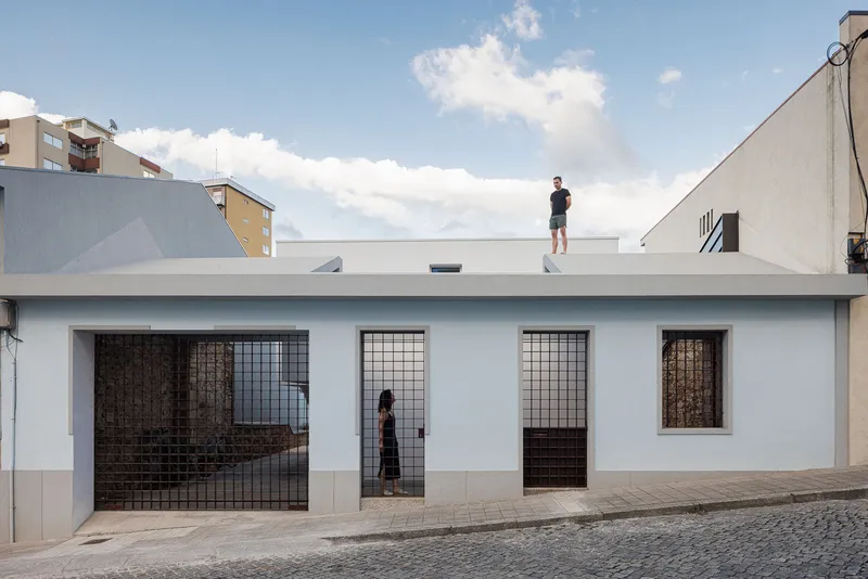 Street facade with white stucco walls and metal grille doors with a figure on the rooftop