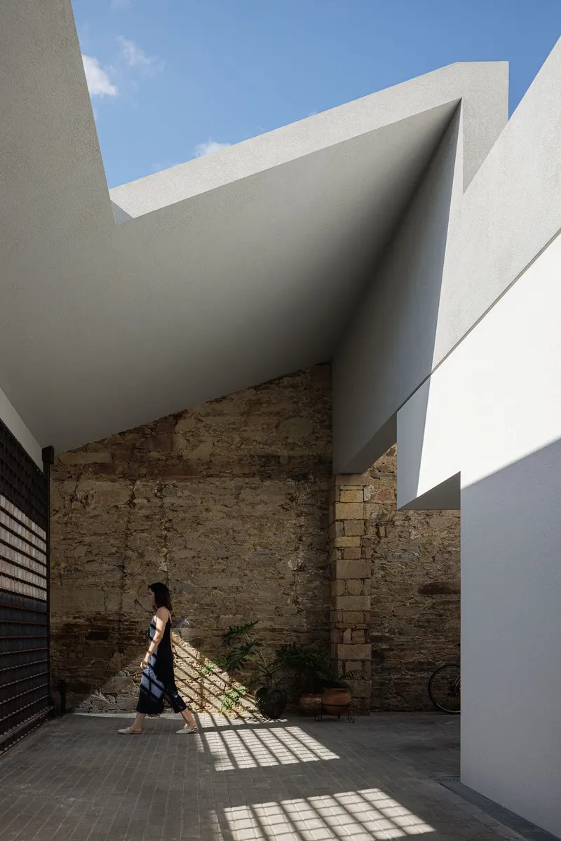 Figure walking through courtyard where gridded screen casts geometric shadows on brick paving