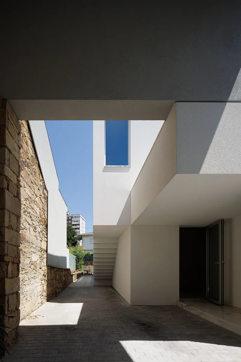View along courtyard passage showing white volumes, exposed stonework and external stair under blue sky