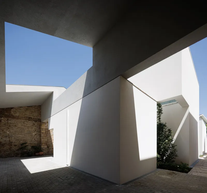 White stucco courtyard with angular volumes and a dark canopy framing blue sky