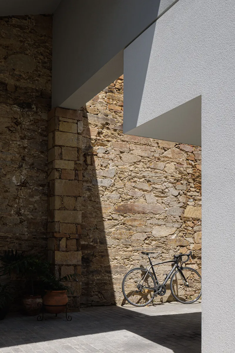 Weathered stone wall alongside white stucco volumes with a bicycle leaning in shadow