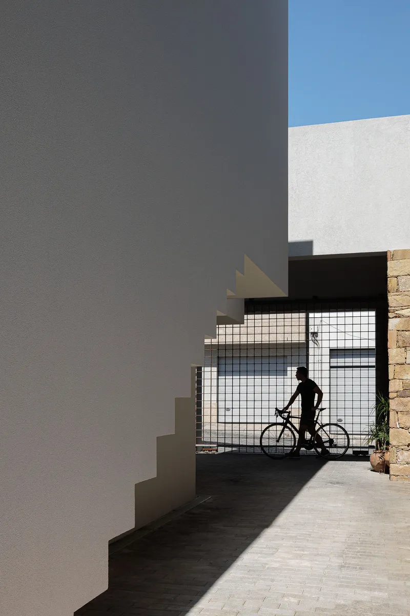 Covered entry passage with gridded glass screen and cyclist silhouetted against bright daylight