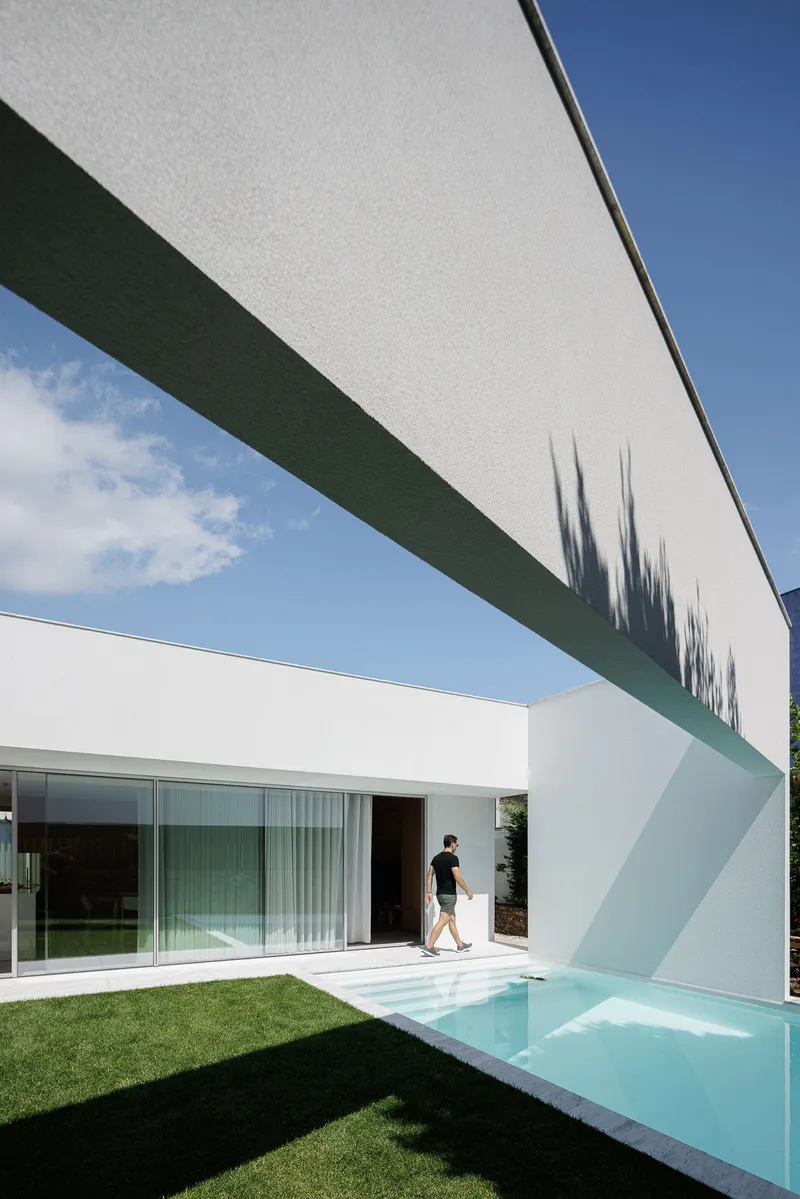 Cantilevered white beam crossing above the pool with person walking past sliding glass doors