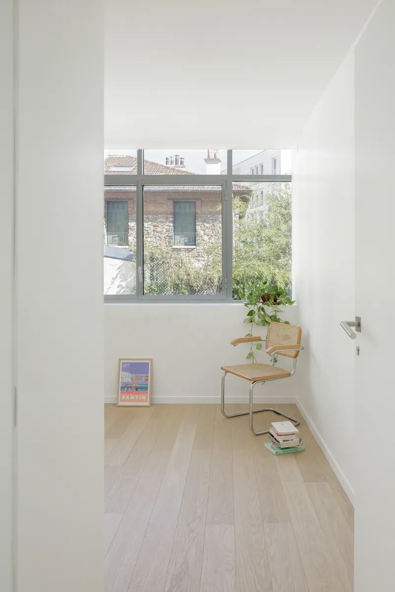 Narrow room with window overlooking a neighboring masonry building and garden in soft daylight