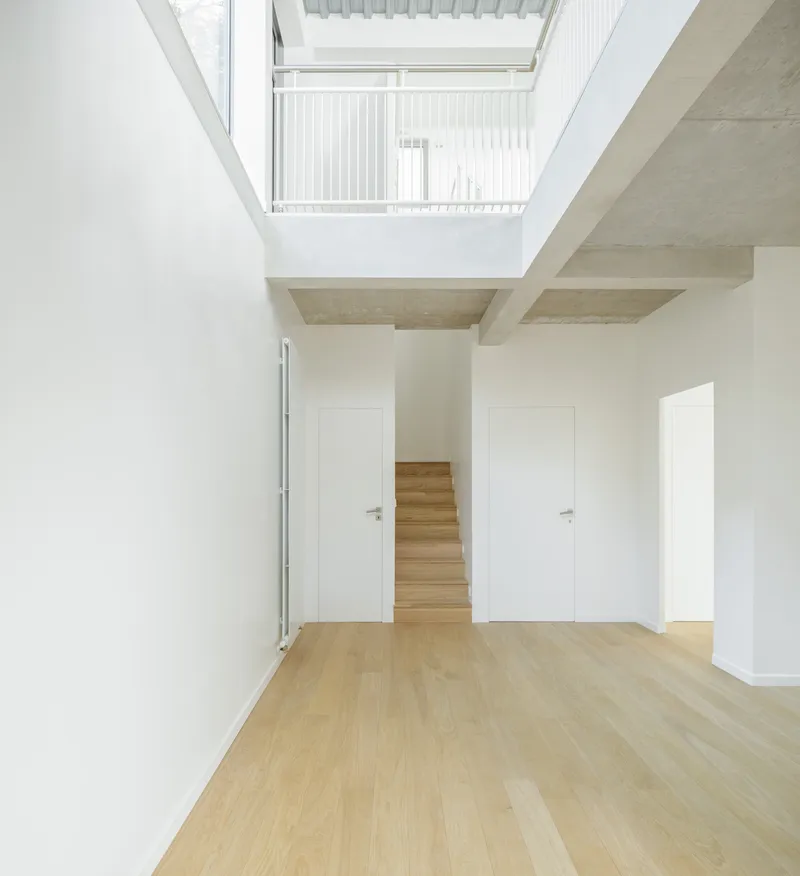 Double-height living space with exposed concrete beams and skylight opening to upper floor balcony