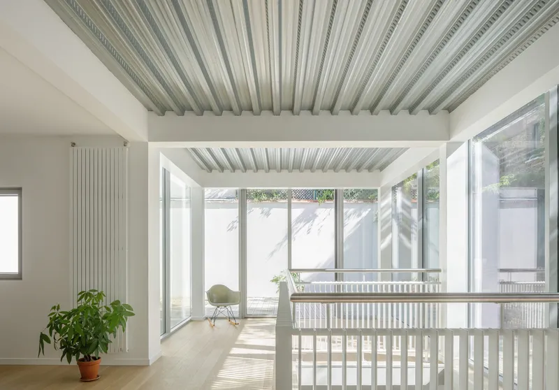 Interior view through white slat railing to glazed courtyard with potted plant and dappled sunlight