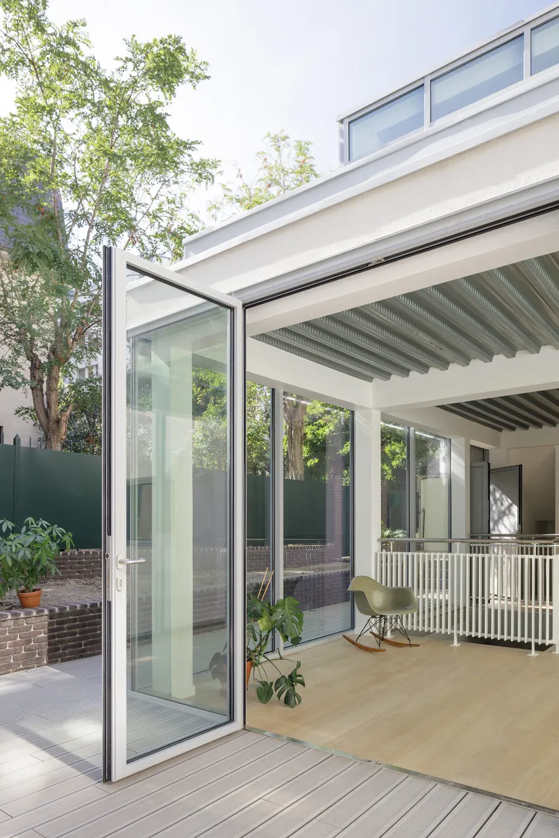 Pivoting glass door opening from interior to timber deck courtyard surrounded by trees and planted beds