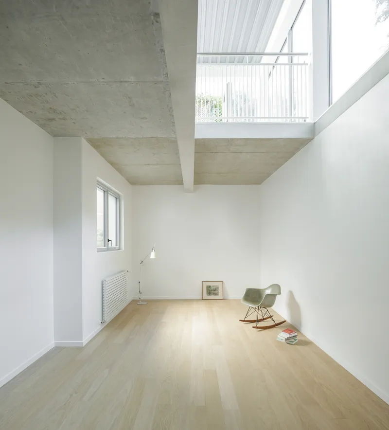 Upper floor room with exposed concrete ceiling beams and clerestory window framing white slat railing above
