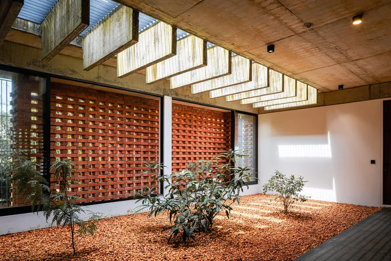 Interior courtyard with perforated red brick walls, planted bed with gravel and exposed concrete ceiling with clerestory