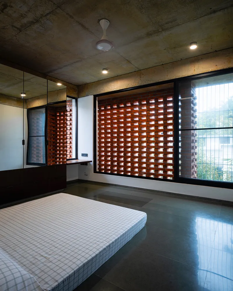 Bedroom with perforated terracotta screen window filtering daylight across polished floor