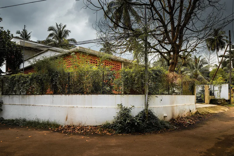 Street view of perforated brick facade behind white boundary wall and leafless tree