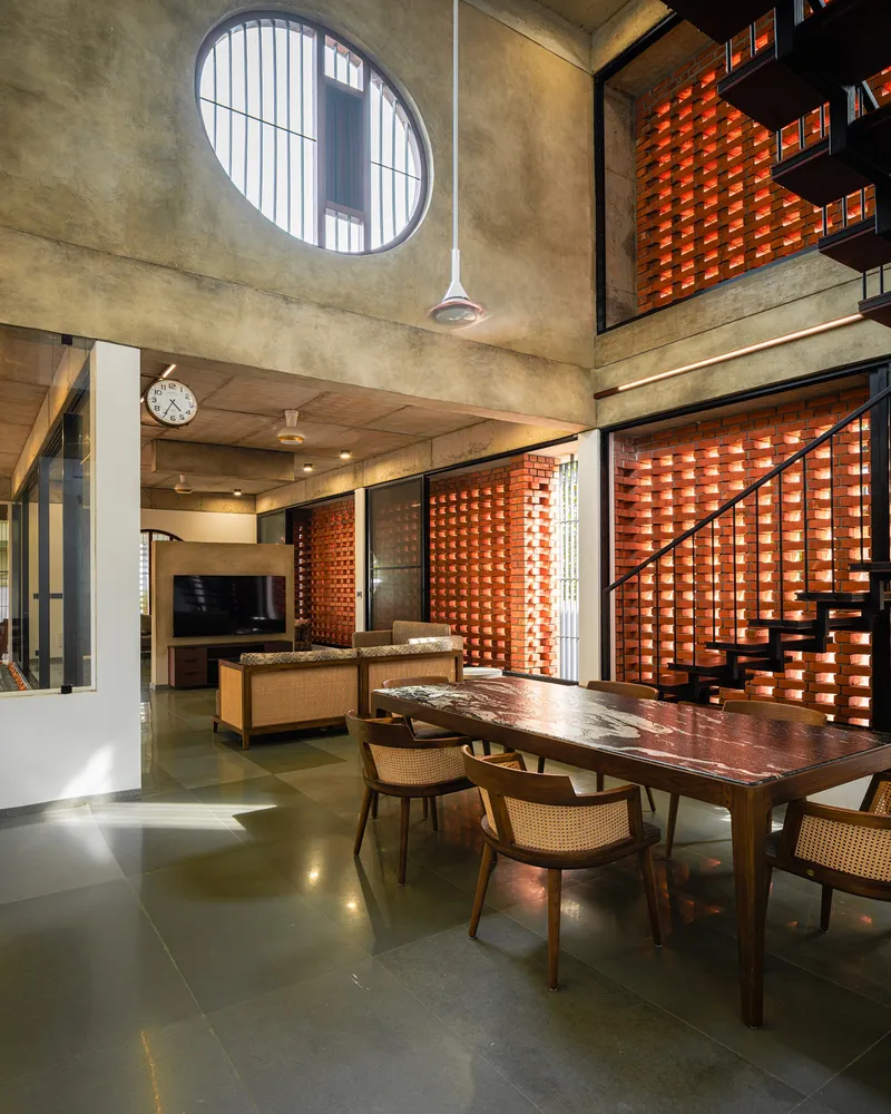 Double-height living and dining space with circular window above and perforated brick screens on two levels