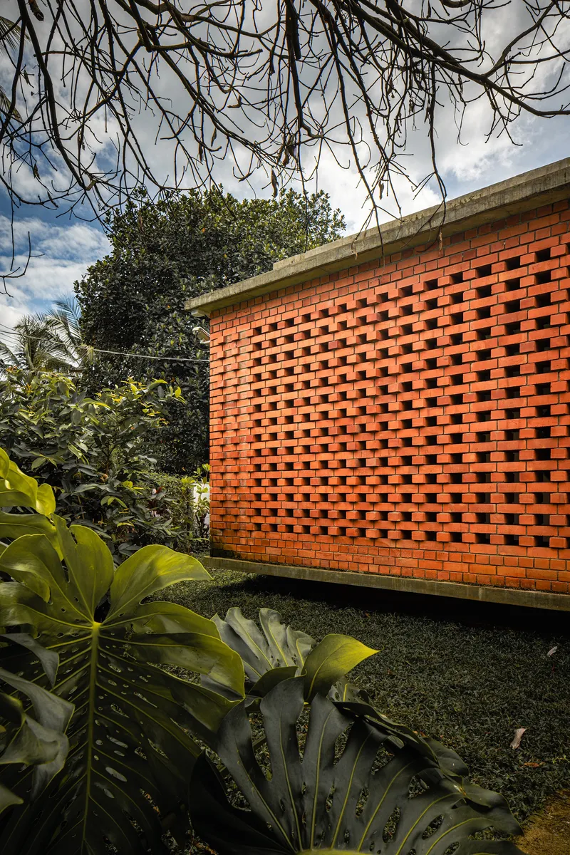 Perforated red brick wall with concrete cap beside planted bed under bare branches