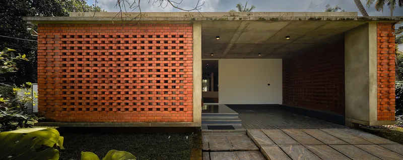 Entry facade with perforated brick volume and open concrete-framed carport under overcast sky
