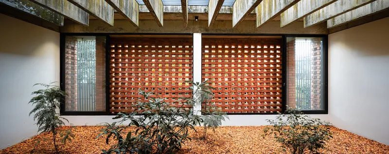 Interior courtyard with orange gravel bed and brick screen wall under timber-beam skylight